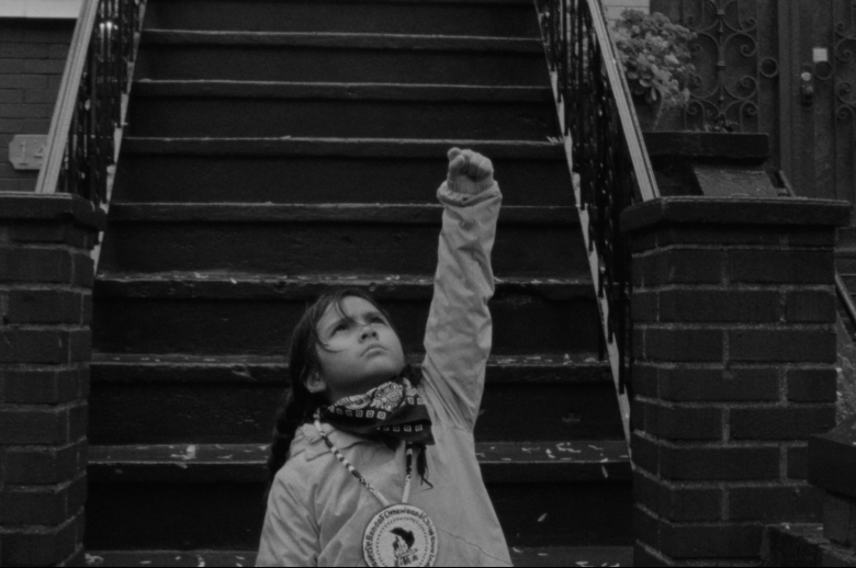 young Anishinaabe girl with raised fist in front of stoop