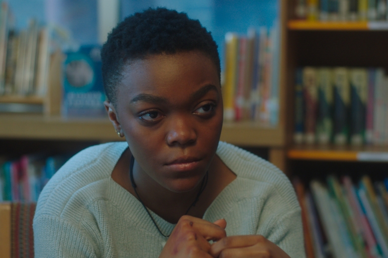 woman sitting in front of bookshelf staring intensely 