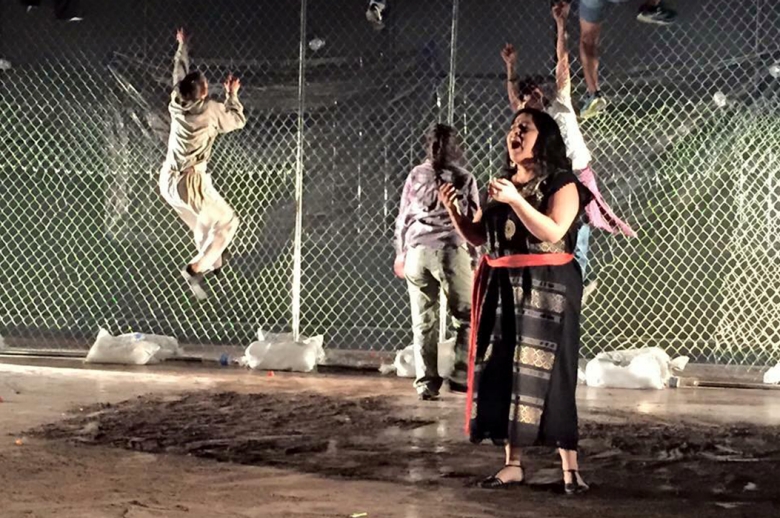 Woman singing while people climb a fence in the background