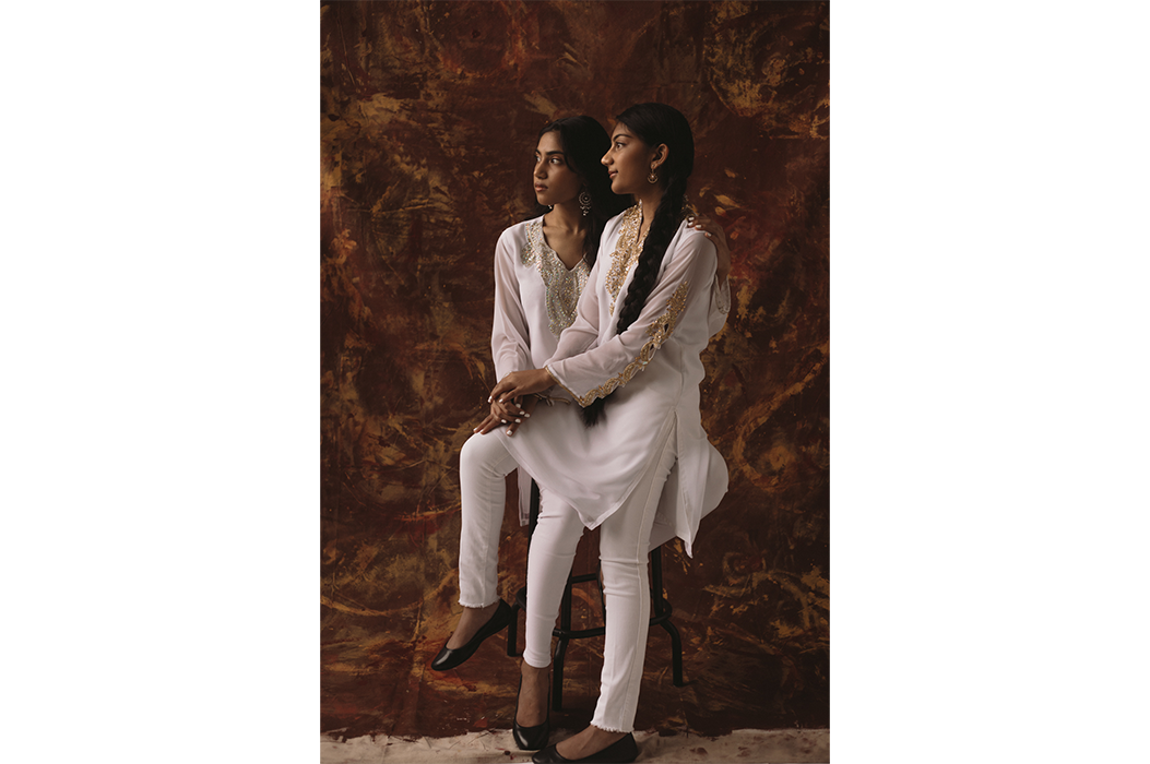 A woman sitting on another woman's lap in front of a brown backdrop