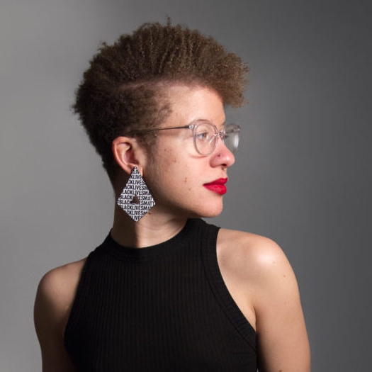 Lindsay Catherine Harris headshot in black sleeveless shirt, she wears glasses, red lipstick and geometric earrings that say Black Lives Matter