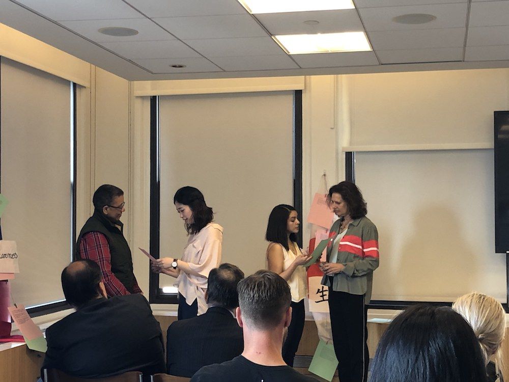 Four women stand at the front of a presentation. Two women read to the other two