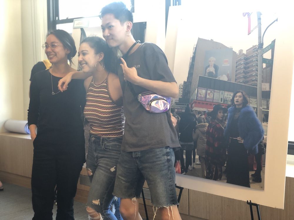 Three people pose together in front of large poster prints of photos of them