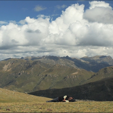 A figure laying on the ground looking up at the sky filled with clouds.