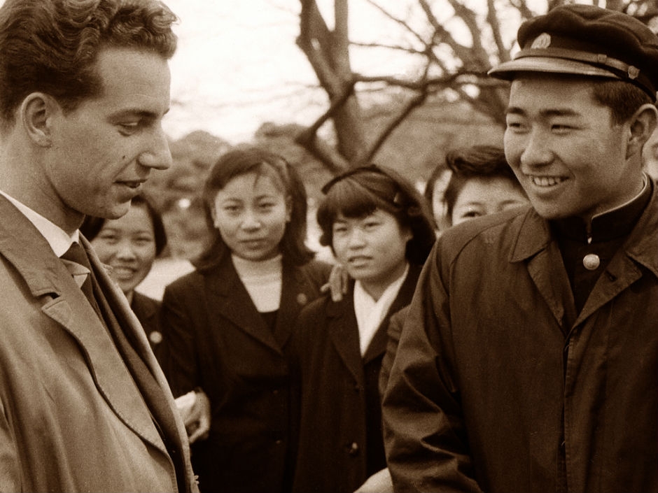 Two men in the foreground, four women in the background looking in at the men talking