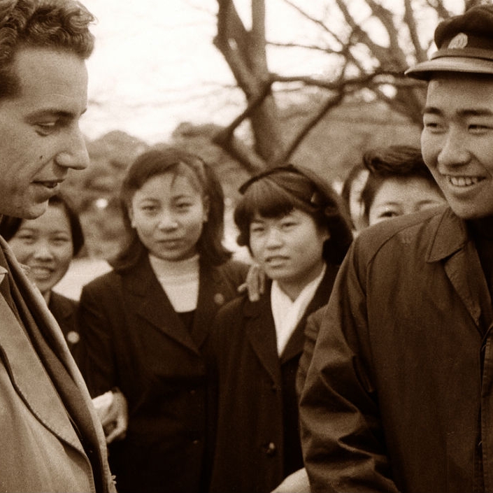 Two men in the foreground, four women in the background looking in at the men talking