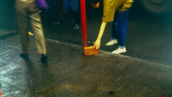 A woman bent low to the ground brushing the sidewalk with a bristle brush.