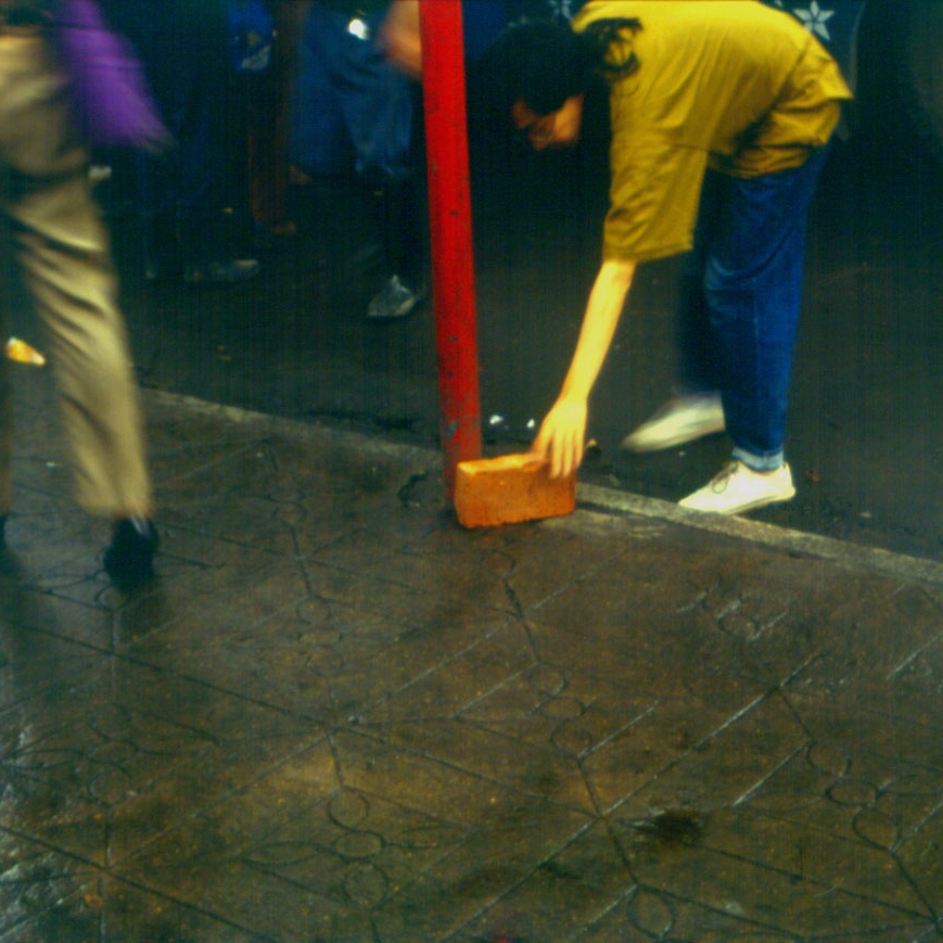 Person wearing a brown shirt bending down with one hand near the ground.