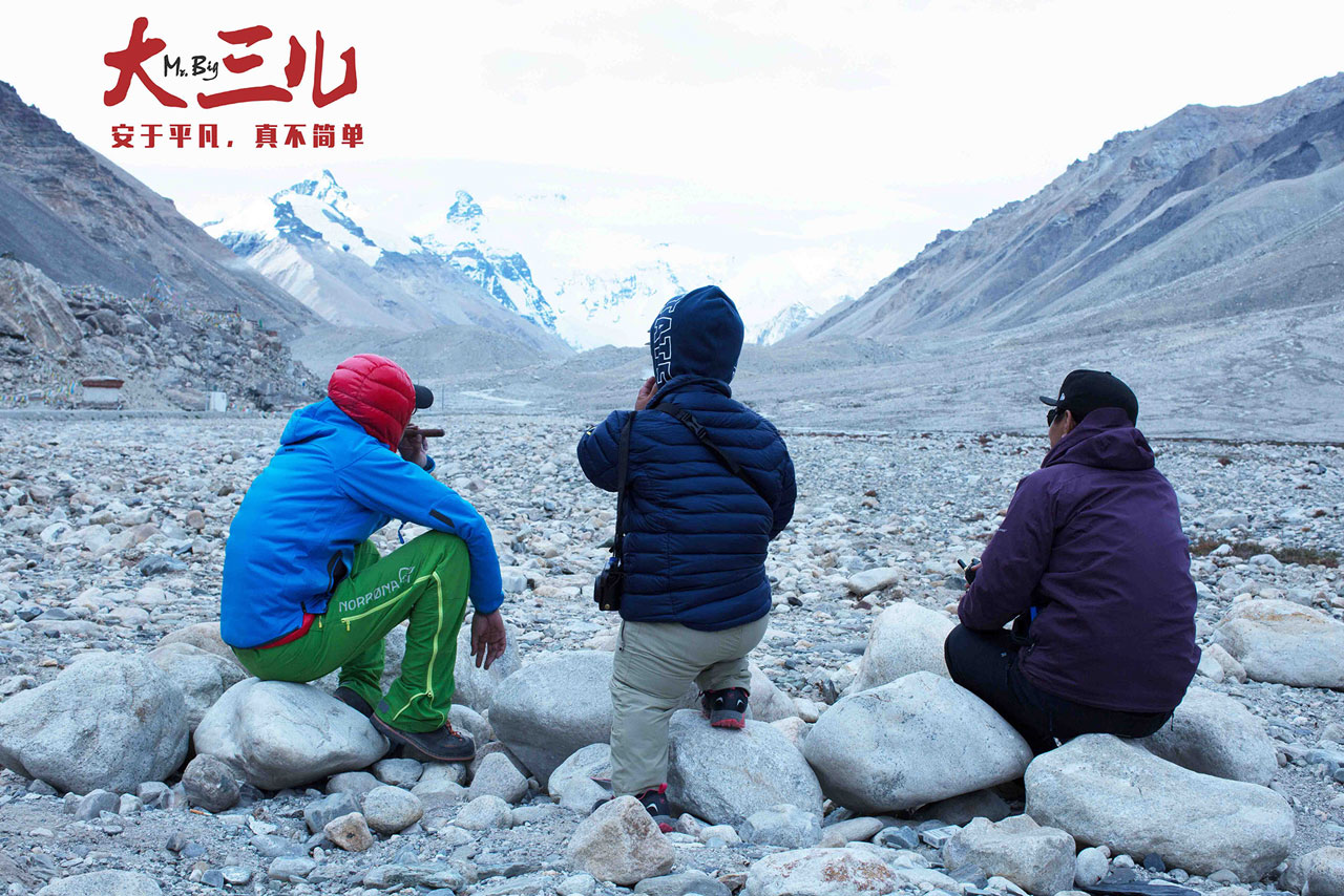 Three men sitting on rocks, with their backs to us