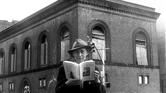 Man wearing a hat, holding a book open, in front of the building for Anthology Film Archives