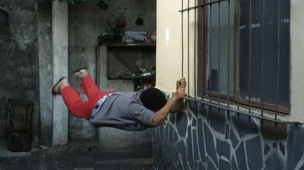 A person hanging from a window grate in mid-motion.