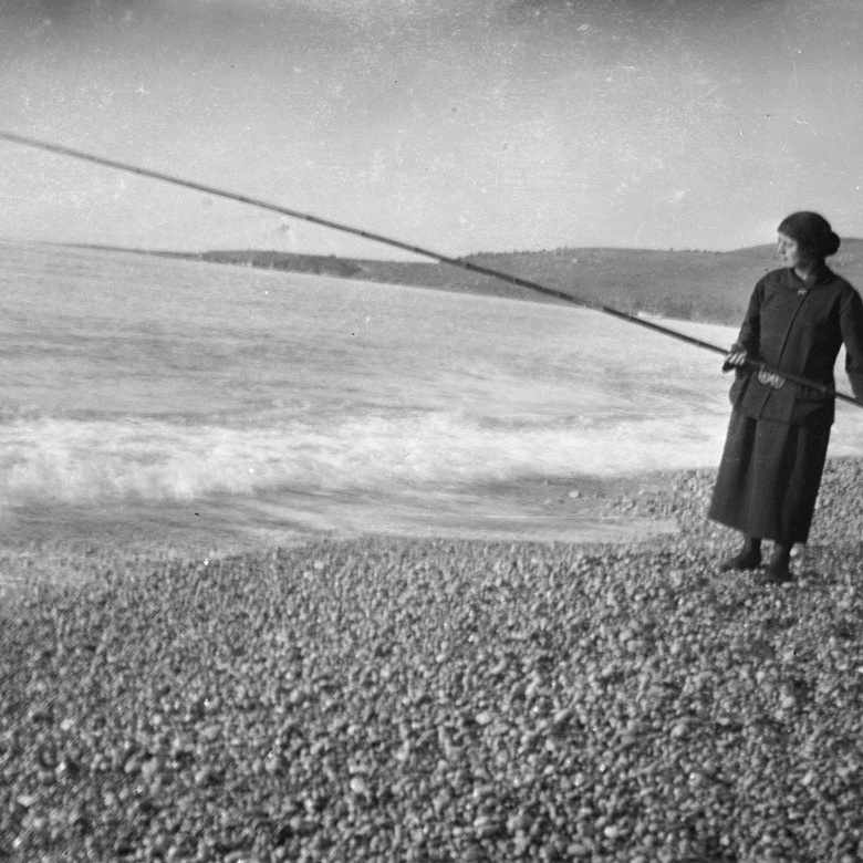 Woman on a beach holding a long pole over the water.