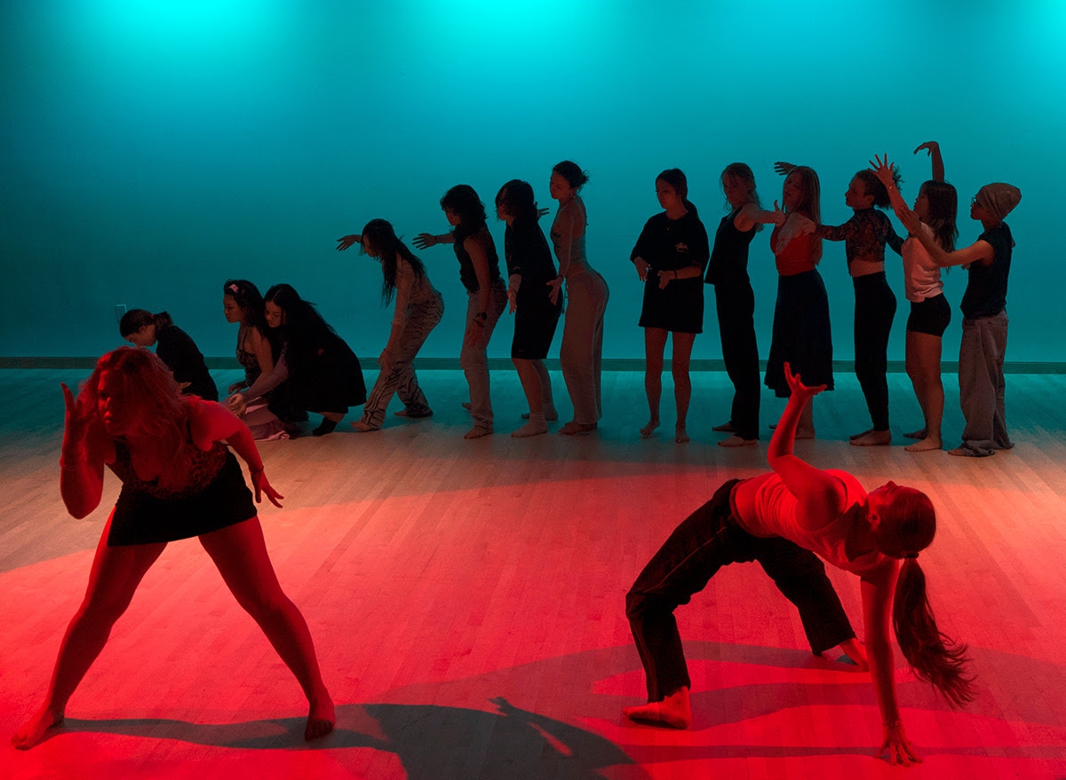 Two students in the foreground extend their bodies in red light, Many students lined up in the background in blue light