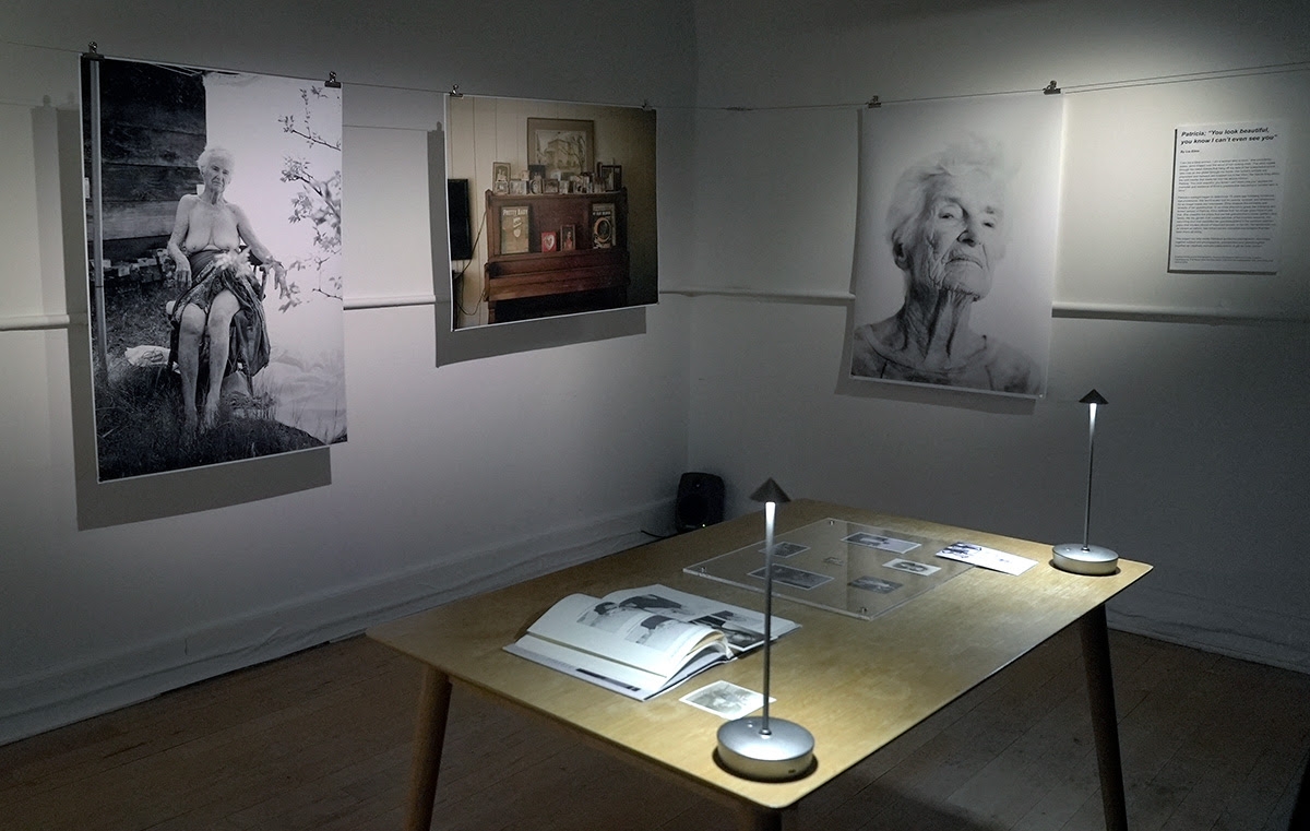 A small gallery features three large photos on the wall, a table in the center of the room displays related objects