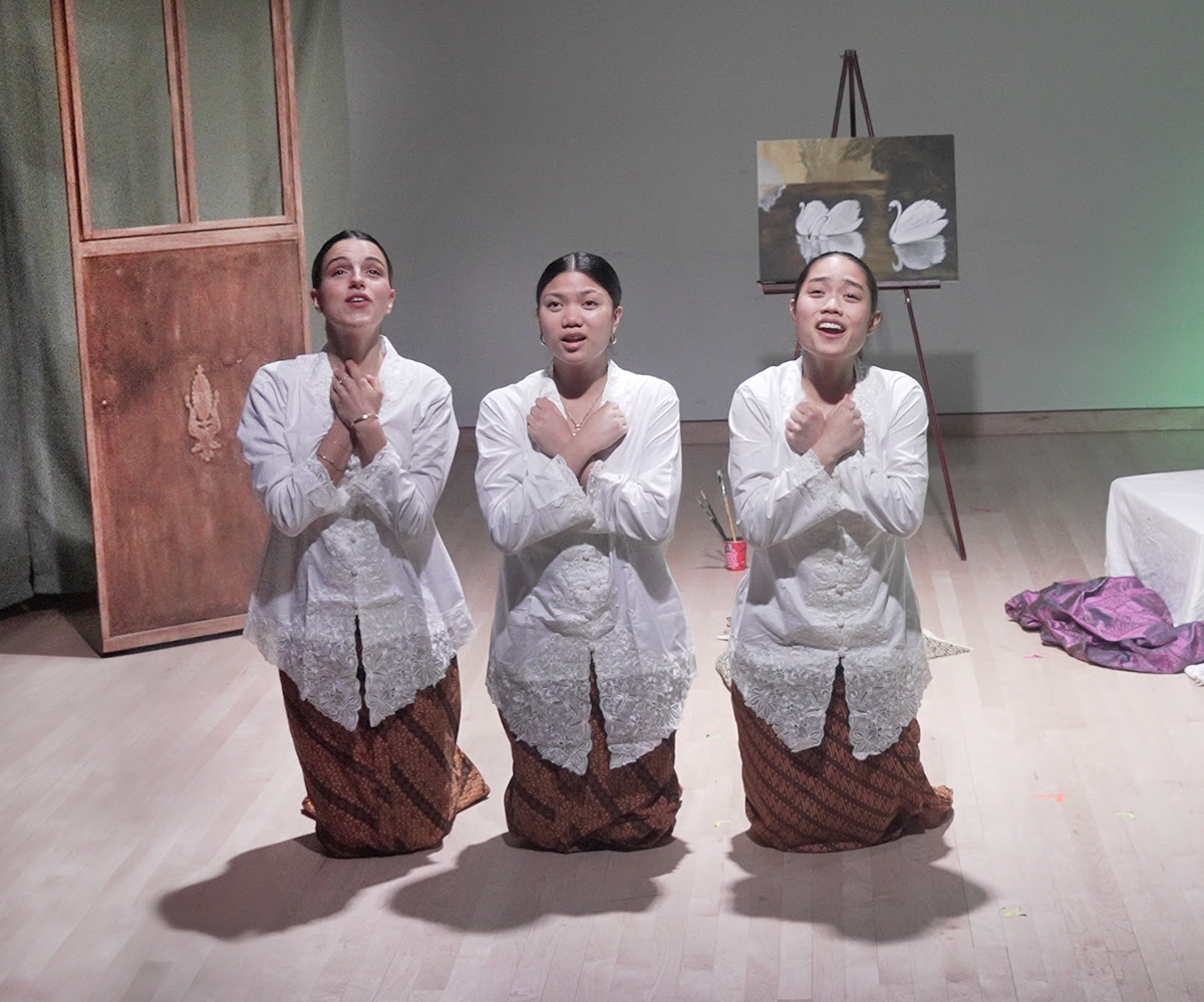 Erika and 2 other performers kneel, hands crossed over their chests, singing