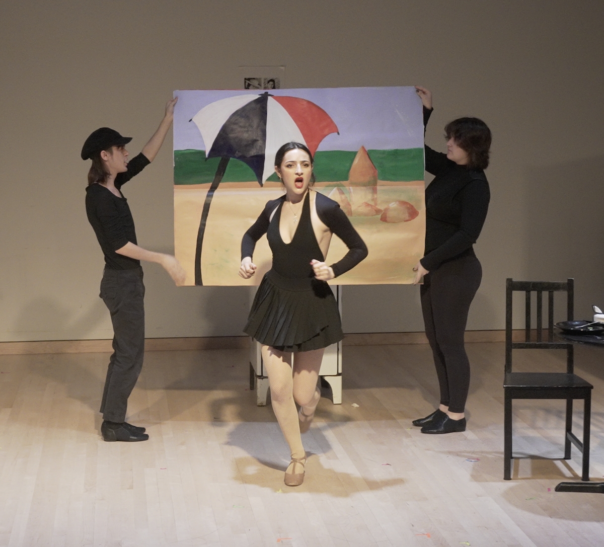 Two performers hold a backdrop poster with a beach as Hunter sings and dances in front of it