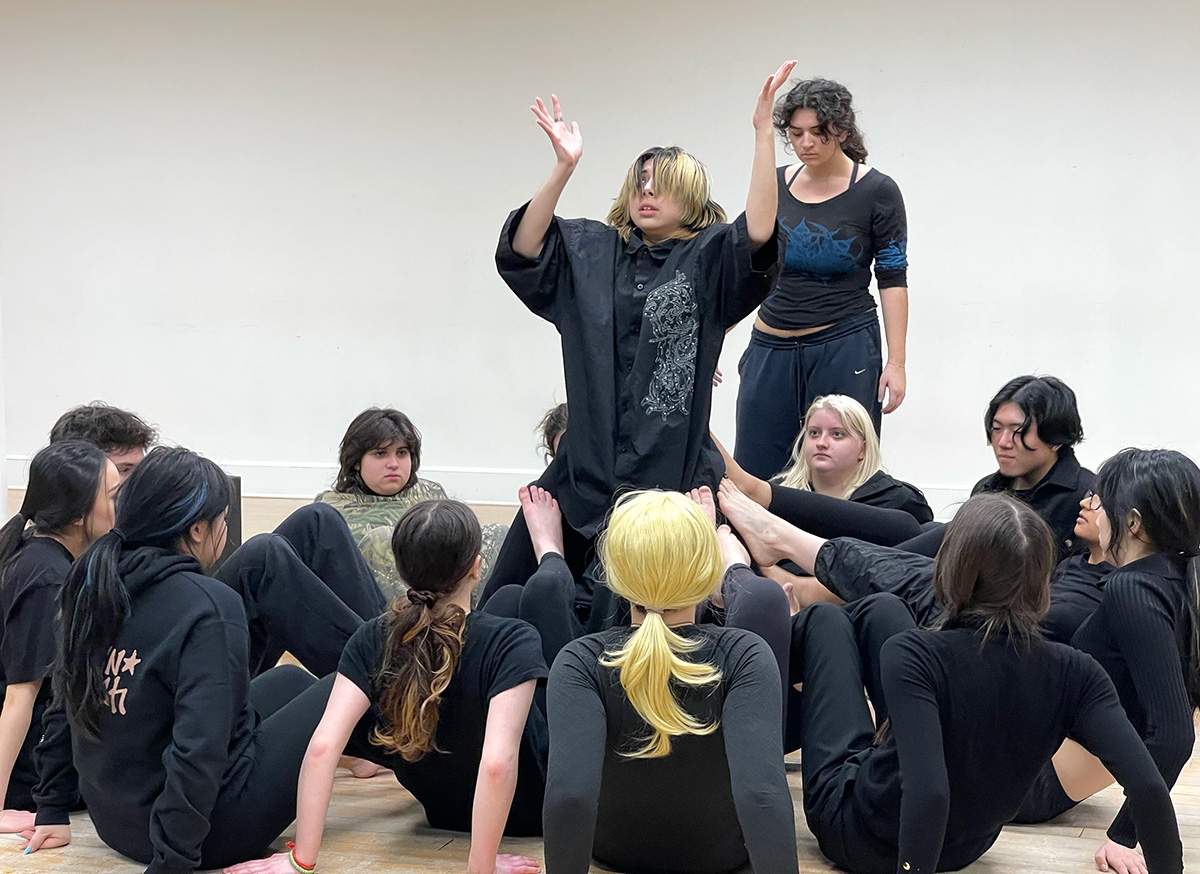 Two students stand posed while many others surround them on the floor