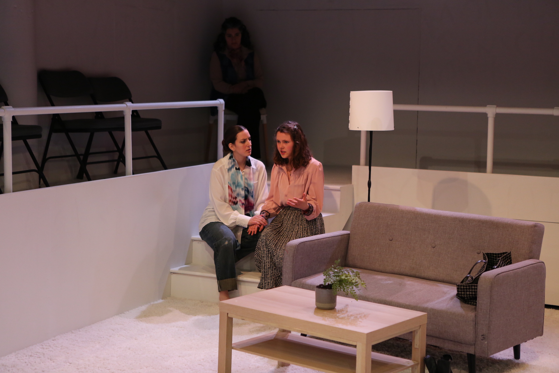 Two women sit in a white carpeted room