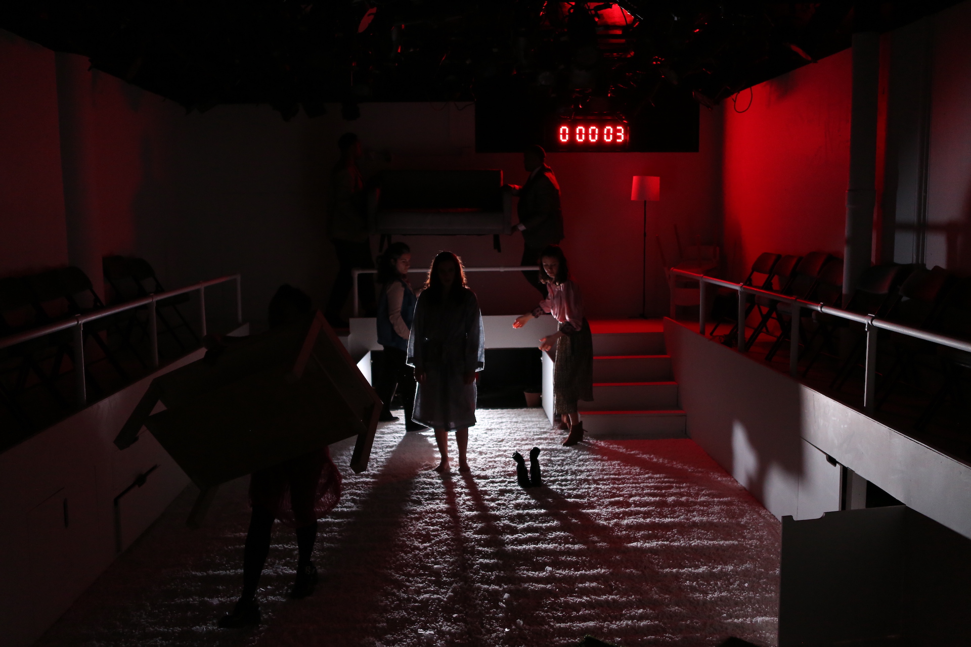 Woman stands in shadow on white carpet with red light and a bright white light behind her