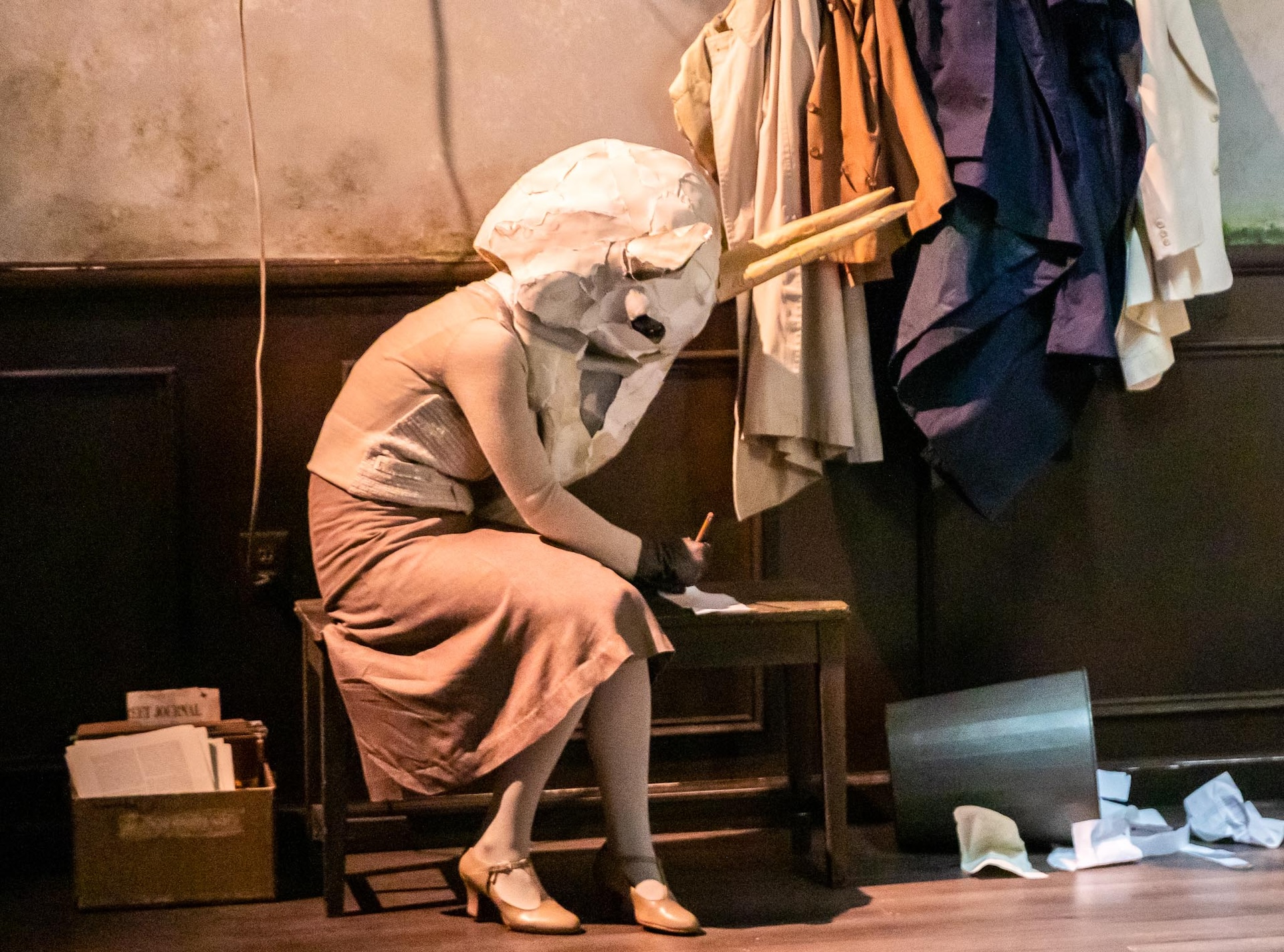 actor from sideview seen sitting down writnig on paper wearing mask