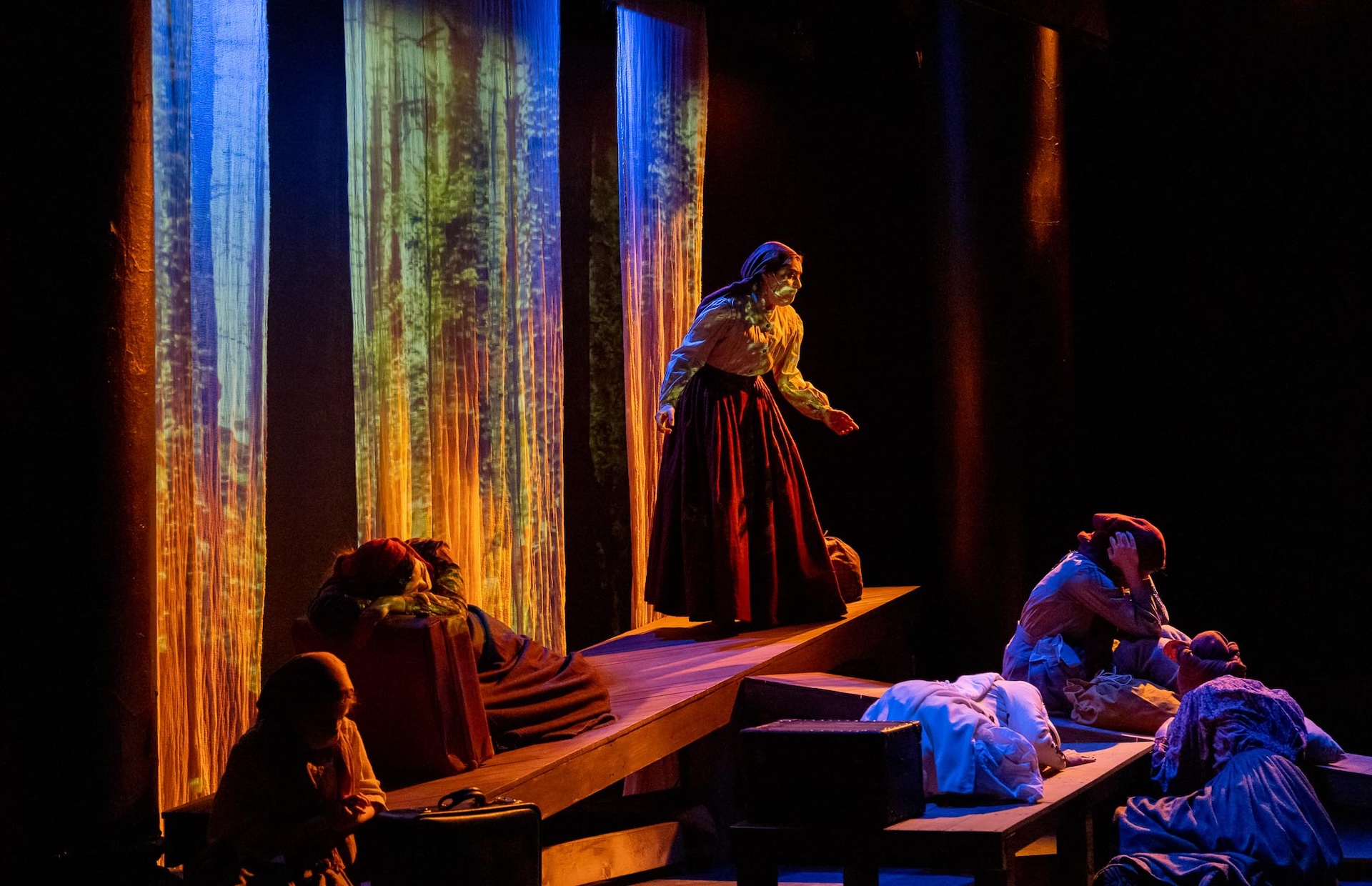 Actors on slanting stage with colourful drapery in the background