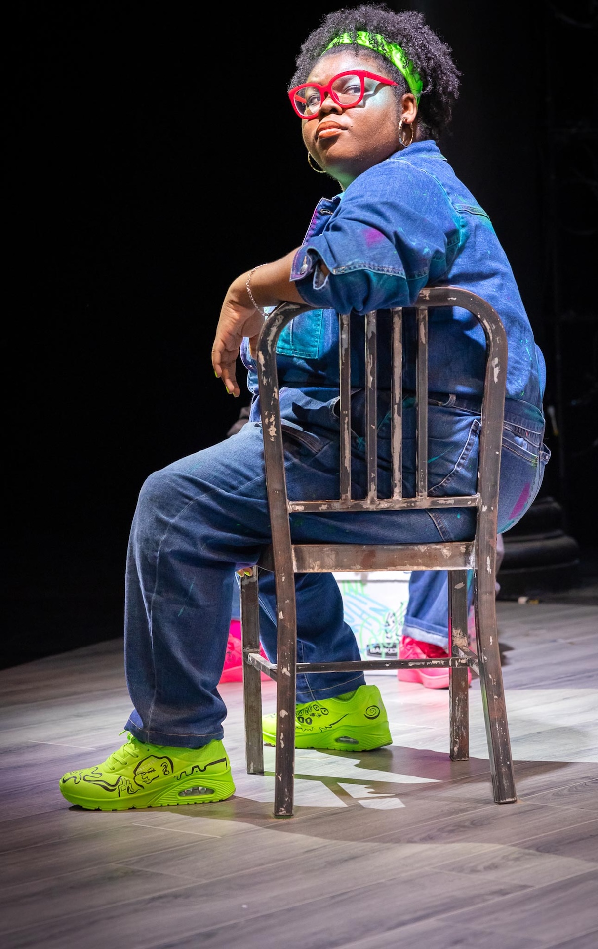 Actor wearing blue jumpsuit sitting on a chair 