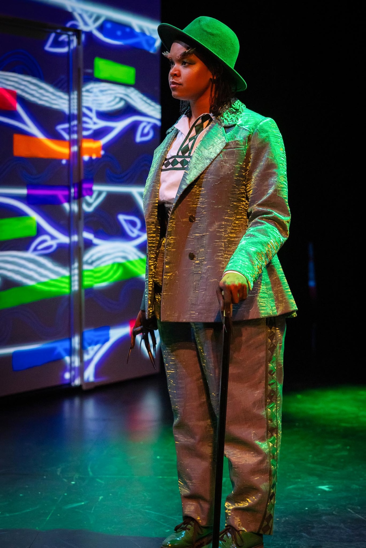 actor wearing suit and bowl hat in front of light display