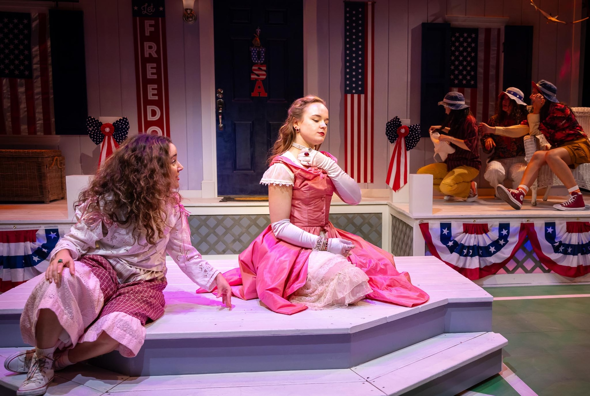 actor talking to other actor wearing a pink dress sitting onstage