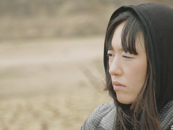 Film Still from A Utopia. Image of woman's face wearing a hoodie.