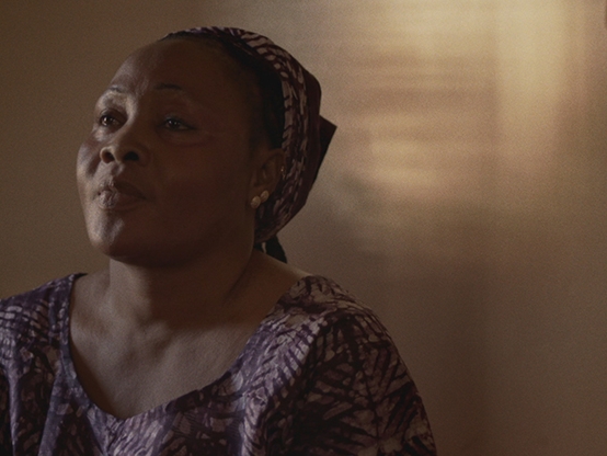 Film Still from Samedi Cinema. Image of woman from shoulders up with scarf around her hair. 