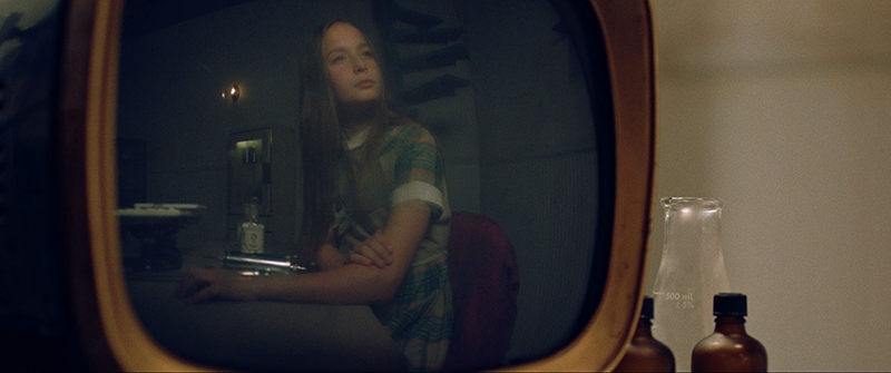 A reflection in a television of a young man sitting in a chair.