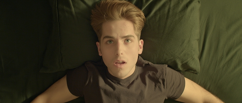 A young man laying down in a bed, looking up at the ceiling.