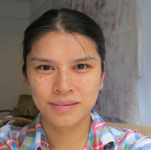 A woman grinning wearing a plaid shirt