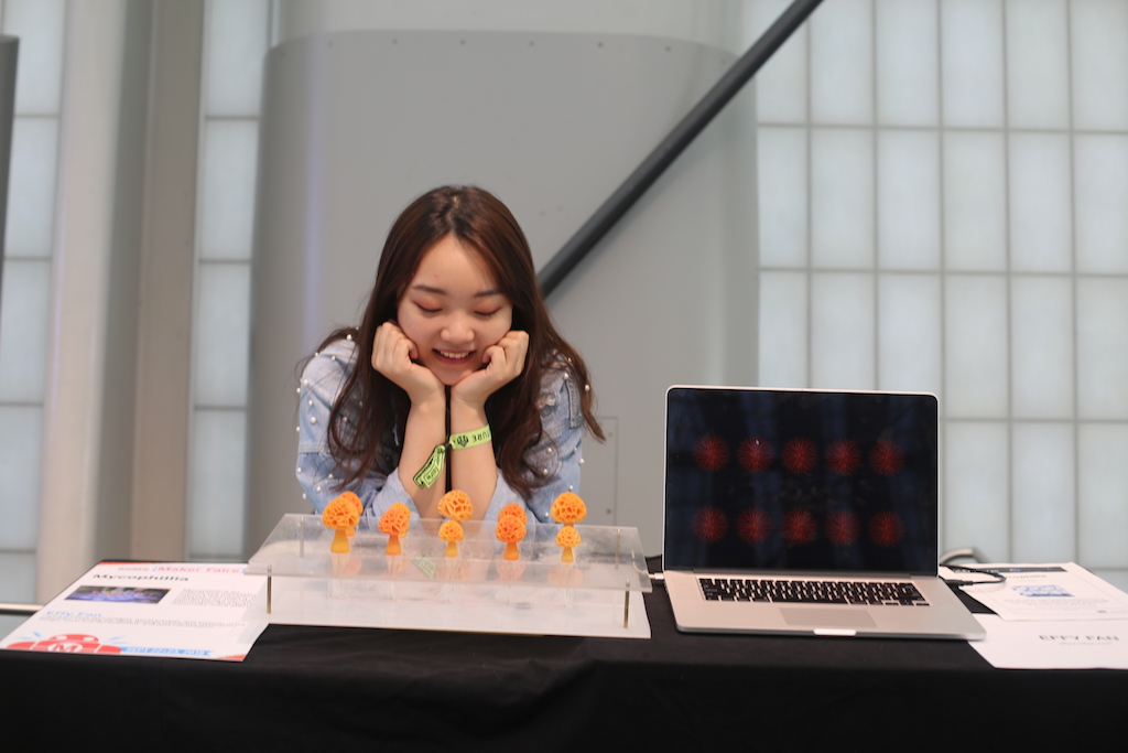 Student smiles down at project of small orange mushrooms