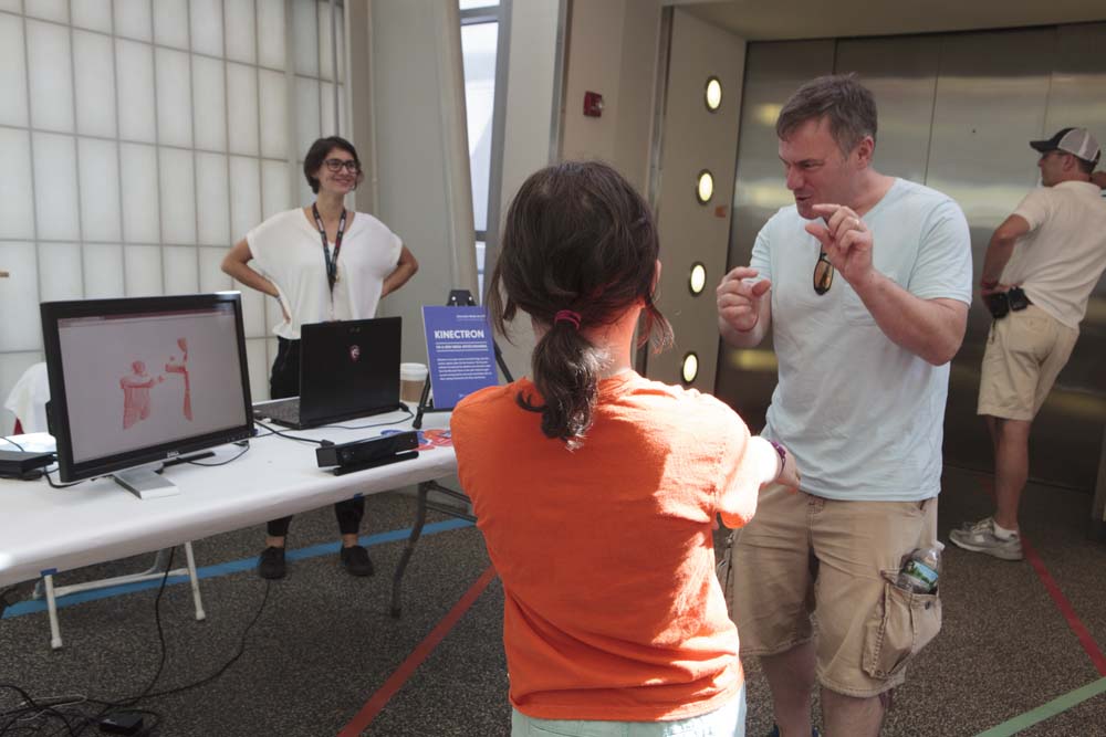 A man and child interact while looking at their 3D wireframe images on a computer screen