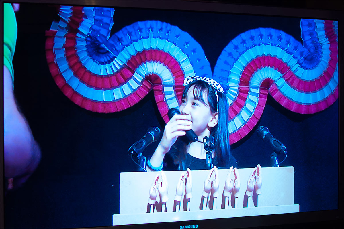 a young girl talking into a microphone with mini hands clapping