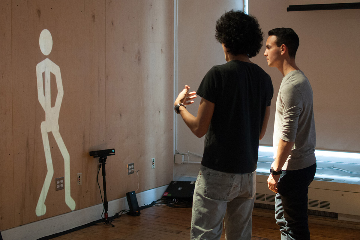 2 people standing while a stick figure is projected onto the wall