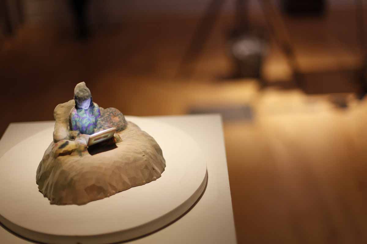 a miniature sculpture of a person sitting in bed with a laptop