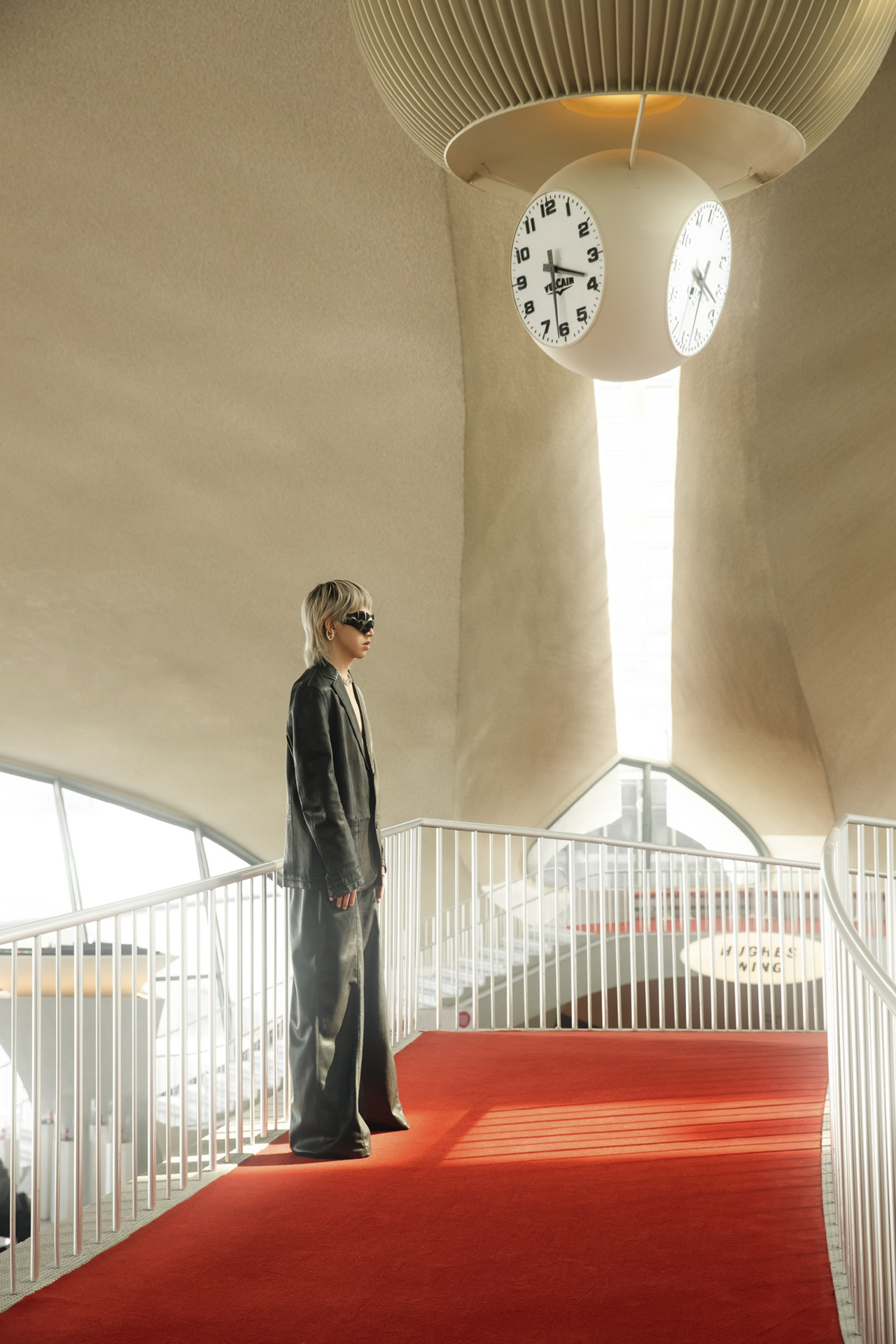 a person stands in black clothing against the red carpet and white walls of a meeting hall