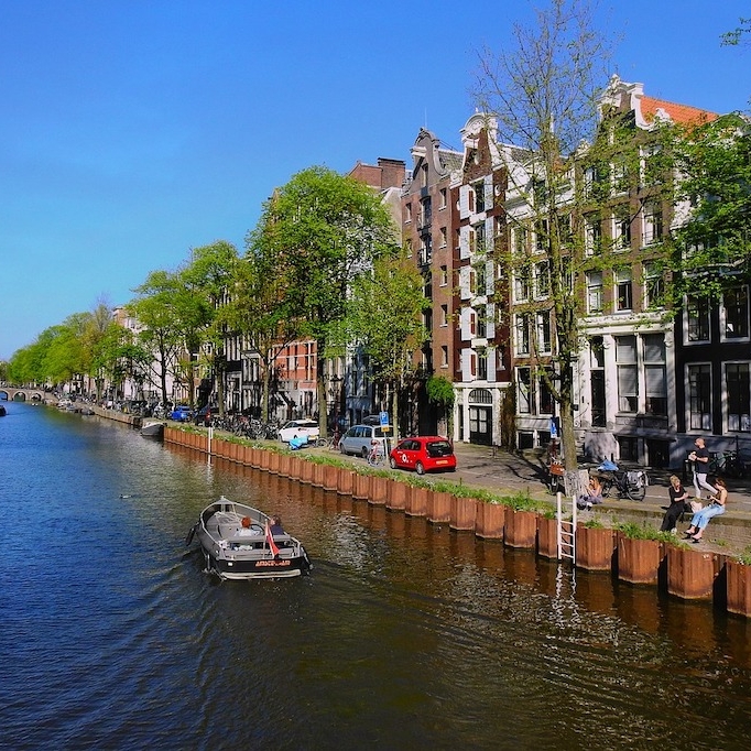 A boat drifts down a canal in Amsterdam during the day.