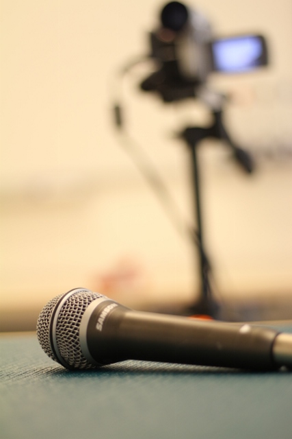 Microphone in the foreground, video camera out of focus in the background.