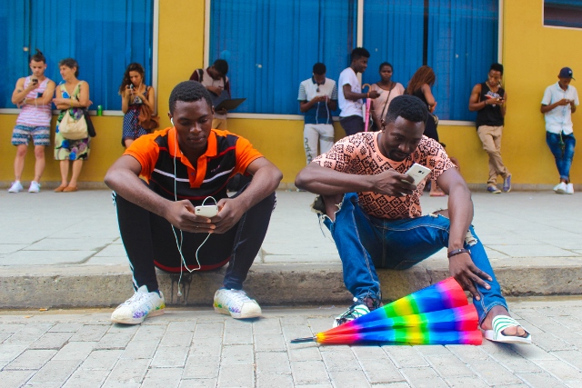 Two men sitting on a curb using their cell phones.