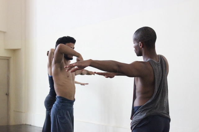 Dancers posing with their arms lifted across their bodies.