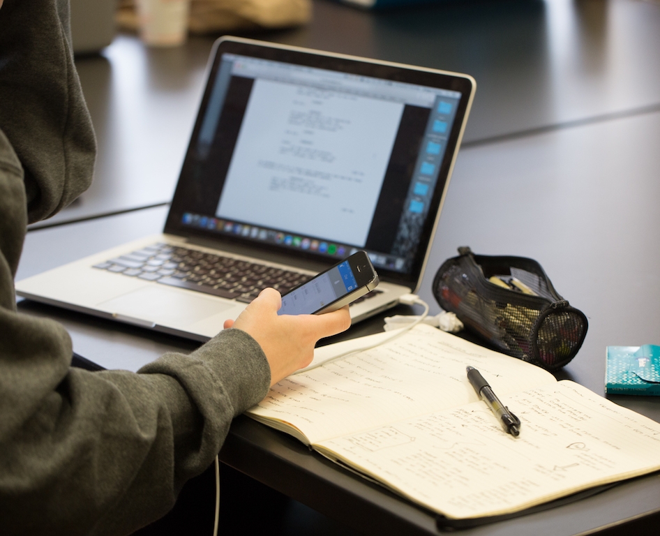 Student holding phone in front of an open laptop