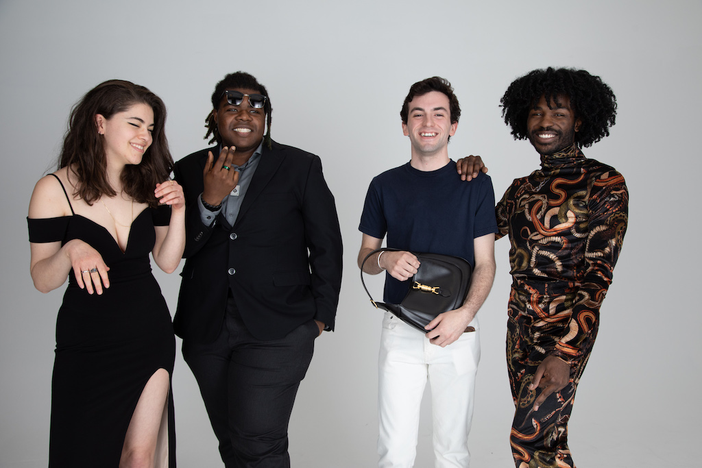 Four students standing, smiling, and posing against a gray photography backdrop