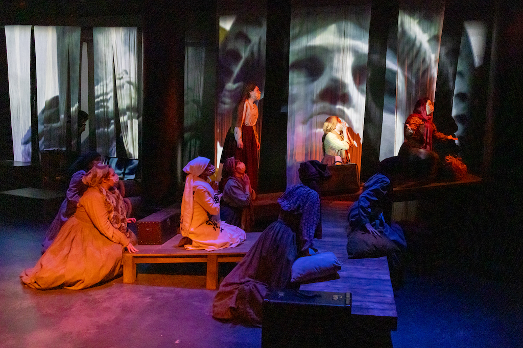 Students seated on risers, mid-performance, with a projection of the Statue of Liberty in the background